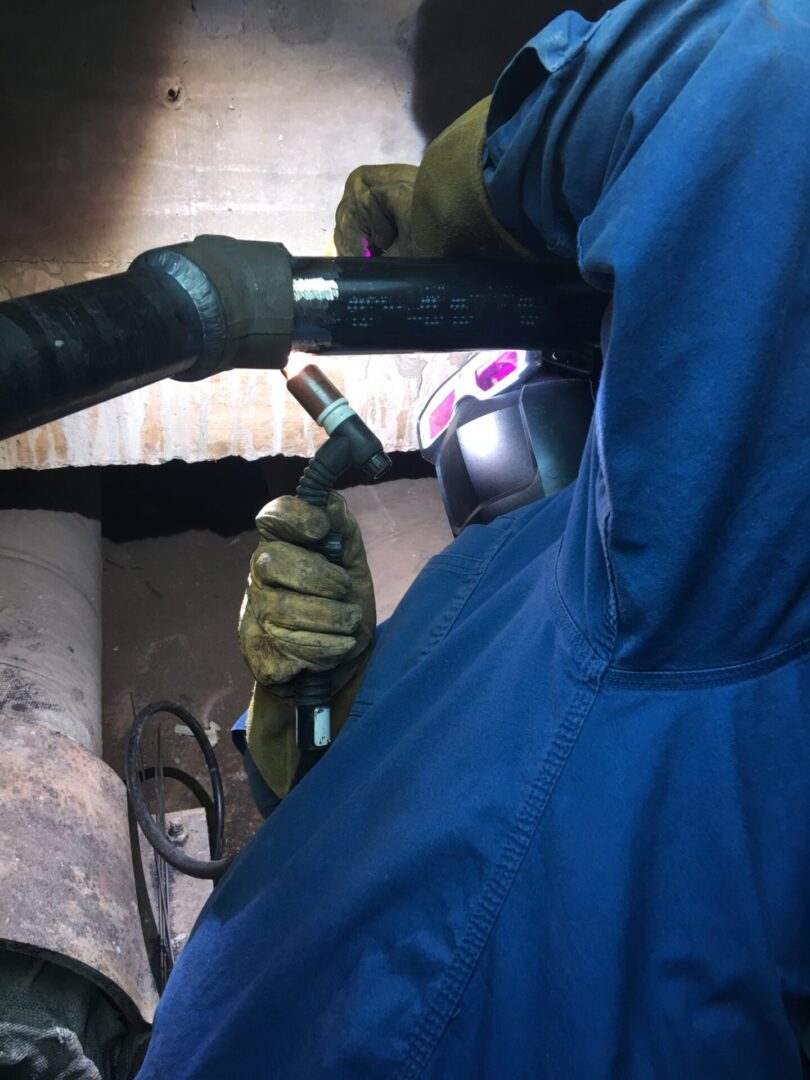 Welder installing steam branch lines inside confined space steam tunnel during industrial piping project