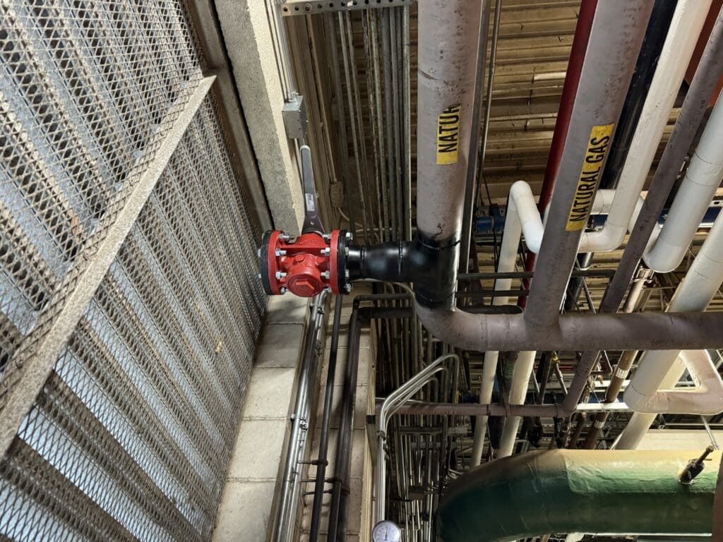 Welder installing butt weld tee, valve, and blind flange on live natural gas piping system